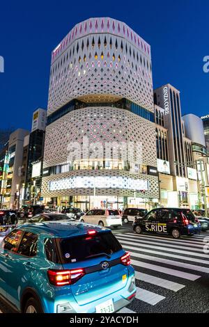 Vue de l'autre côté de la route du bâtiment Ginza place revêtu de blanc illuminé avec le bâtiment Gina Core à côté de lui la nuit. Rue très fréquentée par la circulation Banque D'Images