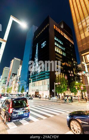 Trafic passant devant le bâtiment Chanel sur la Ginza la nuit. Prise de vue grand angle, lampadaire éblouissant au-dessus de la tête, bâtiments de l'autre côté de la rue. Banque D'Images