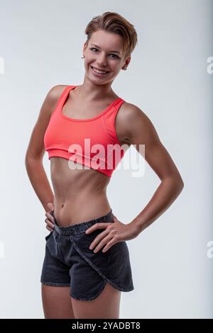 Jeune femme heureuse et confiante en vêtements de sport pose après une séance d'entraînement, rayonnant de joie et de détermination. Son sourire et son énergie inspirent le fitness et le bien-être Banque D'Images