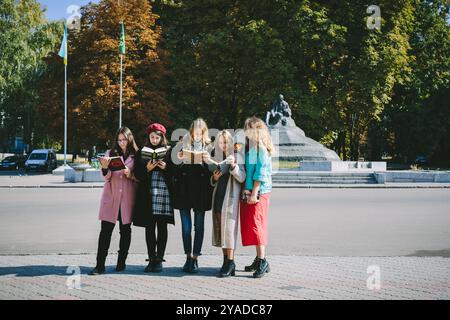 Romny, Ukraine, 29 septembre 2019 : cinq jeunes femmes se tiennent dans la rue et lisent un livre. Banque D'Images