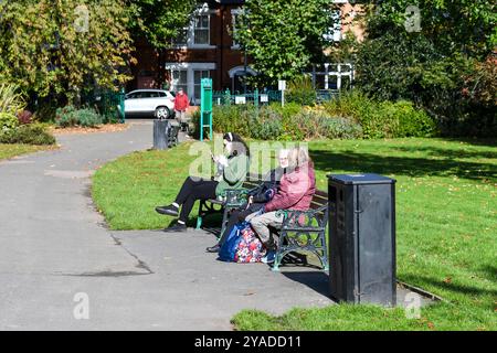 les gens assis sur les bancs du parc queens park loughborough Banque D'Images