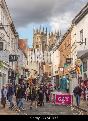 Rue historique de la ville bordée de boutiques et les tours d'une cathédrale s'élevant au-dessus des toits. Un ciel avec des nuages est au-dessus et les piétons sont sur la rue Banque D'Images