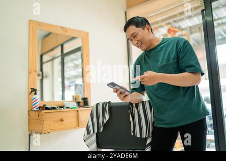 Un homme est debout dans un salon de coiffure, regardant son téléphone Banque D'Images