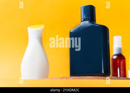 Une collection de bouteilles cosmétiques sur une surface en bois sur un fond jaune vif. L'accent est mis sur une bouteille rectangulaire bleu foncé avec un b blanc Banque D'Images
