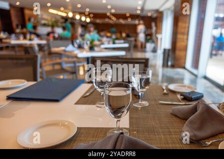 Ensemble de table de restaurant élégant avec des verres avec de l'eau et des assiettes, avec un éclairage doux et des gens dînant dans un fond flou. Mexique. Banque D'Images