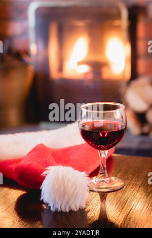 Salon confortable avec verre de vin rouge et chapeau de Santa clause devant la cheminée le matin de Noël 02 Banque D'Images
