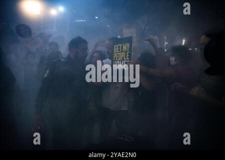 Israël. 12 octobre 2024. Les manifestants et les membres de la famille des otages se tiennent dans la fumée et pointent vers un panneau qui dit : « ramène mon peuple à la maison » devant un policier avec un extincteur. Des partisans ont manifesté avec des membres des familles des otages israéliens contre le premier ministre Benjamin Netanyahou, exigeant un accord immédiat sur les otages et un cessez-le-feu devant le siège des FDI. Tel Aviv, Israël. 12 octobre 2024. (Matan Golan/Sipa USA). Crédit : Sipa USA/Alamy Live News Banque D'Images