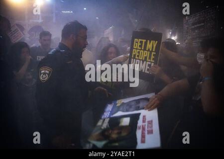 Israël. 12 octobre 2024. Les manifestants et les membres de la famille des otages se tiennent dans la fumée et pointent vers un panneau qui dit : « ramène mon peuple à la maison » devant un policier avec un extincteur. Des partisans ont manifesté avec des membres des familles des otages israéliens contre le premier ministre Benjamin Netanyahou, exigeant un accord immédiat sur les otages et un cessez-le-feu devant le siège des FDI. Tel Aviv, Israël. 12 octobre 2024. (Matan Golan/Sipa USA). Crédit : Sipa USA/Alamy Live News Banque D'Images