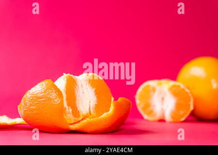Deux oranges sur un fond rose vif, une orange est partiellement pelée, mettant en valeur son intérieur juteux. Les couleurs vives créent un contraste saisissant, Banque D'Images