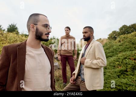 Trois beaux hommes modélisent des tenues d'automne à la mode dans un champ pittoresque entouré par la nature. Banque D'Images