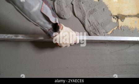 Le travailleur de la construction utilise la règle droite en aluminium pour niveler le mortier de béton qu'il a précédemment appliqué sur le mur. Banque D'Images