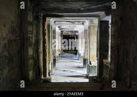 Couloir sombre et en décomposition dans un bâtiment abandonné, murs en ruine et débris dispersés sur le sol. Banque D'Images