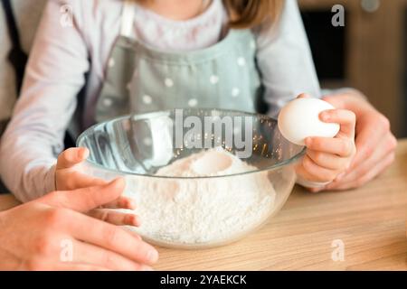 Petite fille craquer l'œuf au bol, aidant le père avec la pâtisserie de cuisson Banque D'Images