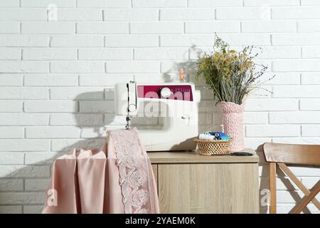 Commode avec machine à coudre, tissu, fleurs en vase et outils à l'atelier Banque D'Images