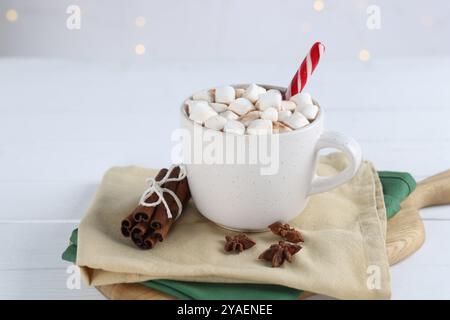 Cacao délicieux avec guimauves et canne à bonbons dans la tasse et épices sur la table en bois blanc Banque D'Images