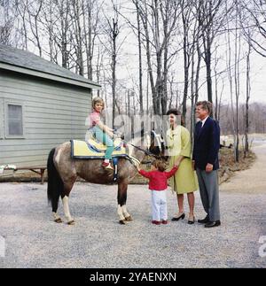 Le président américain John F. Kennedy et la première dame américaine Jacqueline Kennedy se tiennent debout avec leurs enfants, Caroline Kennedy, assis sur son poney, 'Macaroni', et John F. Kennedy, Jr, Camp David, comté de Frederick, Maryland, USA, Robert Knudsen, photographies de la Maison Blanche, 31 mars 1963 Banque D'Images