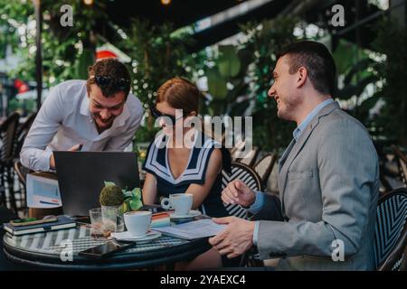 Hommes d'affaires s'engageant dans une réunion en plein air animée dans un café avec un ordinateur portable, mettant en valeur le travail d'équipe et la collaboration dans un cadre détendu et rafraîchissant Banque D'Images