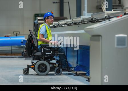 Ingénieur de ligne de production avec handicap dans une usine avec gilet jaune et casque bleu au travail. Banque D'Images