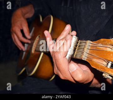 Gros plan de la main et de la glissière en acier jouant une vieille guitare acoustique la nuit. Banque D'Images