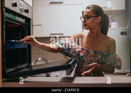 Femme cuisinant dans la cuisine moderne ajustant la température du four Banque D'Images