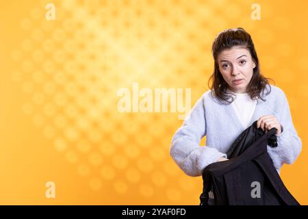 Portrait de femme foudroyant à travers le sac à dos, isolé sur fond jaune de studio. Étudiant sortant des fournitures scolaires du sac à dos utilisé pour se rendre à l'université Banque D'Images