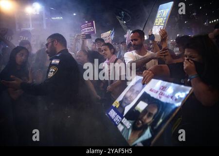 Tel Aviv, Israël. 12 octobre 2024. Les manifestants et les membres de la famille de l'otage se tiennent dans la fumée et pointent vers une pancarte qui dit : « ramène mon peuple à la maison » devant un policier avec un extincteur pendant la manifestation. Des partisans ont manifesté avec des membres des familles des otages israéliens contre le premier ministre Benjamin Netanyahou, exigeant un accord immédiat sur les otages et un cessez-le-feu devant le siège des FDI. (Crédit image : © Matan Golan/SOPA images via ZUMA Press Wire) USAGE ÉDITORIAL SEULEMENT! Non destiné à UN USAGE commercial ! Banque D'Images