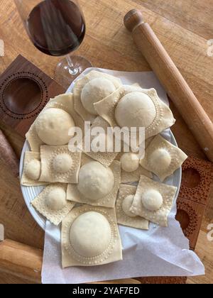 Raviolis faits maison dans une cuisine rustique avec rouleau à pâtisserie, moule et un verre de vin rouge, capturant l'essence de la cuisine italienne traditionnelle Banque D'Images