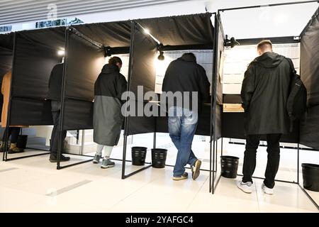 Vilnius, Lituanie. 13 octobre 2024. Les électeurs se préparent à voter dans un bureau de vote pour les élections législatives à Vilnius, Lituanie, 13 octobre 2024. Le premier tour des élections législatives lituaniennes a commencé dimanche, avec des électeurs qui devaient élire 141 membres au Seimas, le parlement monocaméral du pays, pour un mandat de quatre ans. Selon la Commission électorale centrale (VRK), 1 740 candidats sont en compétition pour les élections. Crédit : Alfredas Pliadis/Xinhua/Alamy Live News Banque D'Images