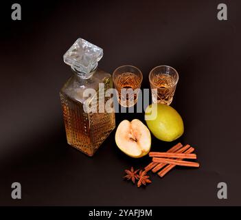 Liqueur de poire à la cannelle et à l'anis, alcool maison dans un bol en cristal sur fond noir, à côté de fruits mûrs et d'épices. Gros plan. Banque D'Images