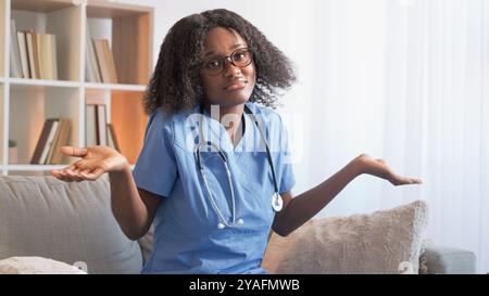Docteur confus. Le doute médical. Incertaine femme infirmière en uniforme clinique haussant les épaules incertaine avec le diagnostic du traitement sur le canapé à l'hôpital. Banque D'Images
