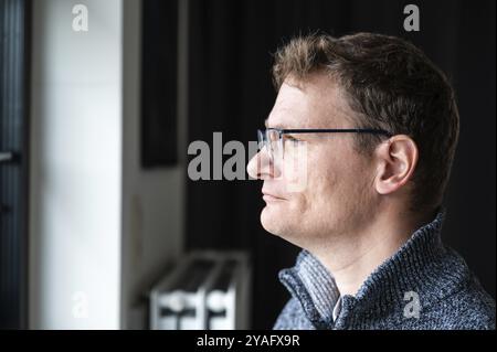 Portrait d'intérieur d'un homme blanc de 45 ans regardant par sa fenêtre à la maison, Bruxelles, Belgique. Autorisation du modèle Banque D'Images