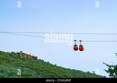 Deux téléphériques sont suspendus à des fils avec une colline verte luxuriante et un fort en arrière-plan à jaipur, en inde Banque D'Images