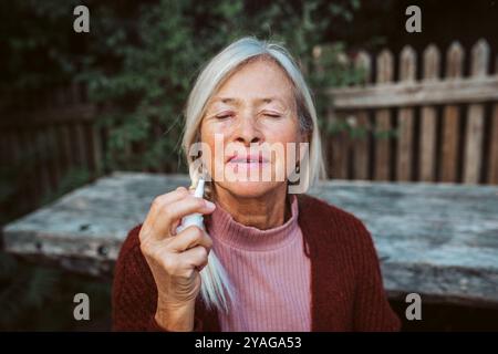 Femme âgée se sentant malade, en utilisant le spray nasal pour aider à la congestion, la boursouflure. Banque D'Images