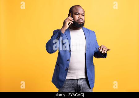 Homme triste ayant le visage de pouting après s'être disputé avec des amis pendant l'appel téléphonique, isolé sur fond de studio. Personne sombre de mauvaise humeur après avoir reçu de mauvaises nouvelles pendant une conversation téléphonique Banque D'Images