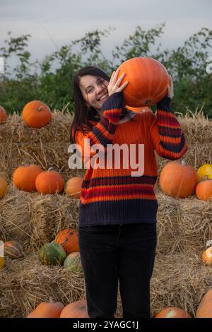 Femme tenant une citrouille assise sur des balles de foin Banque D'Images