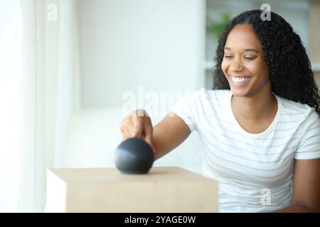 Femme noire heureuse utilisant le haut-parleur intelligent poussant le bouton à la maison Banque D'Images