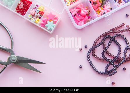 Diverses fournitures d'artisanat sont affichées sur un fond rose, y compris des perles colorées, des ciseaux et des accessoires organisés prêts pour le projet créatif Banque D'Images