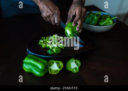 Homme tranchant le poivron vert sur une surface sombre avec un couteau. Banque D'Images