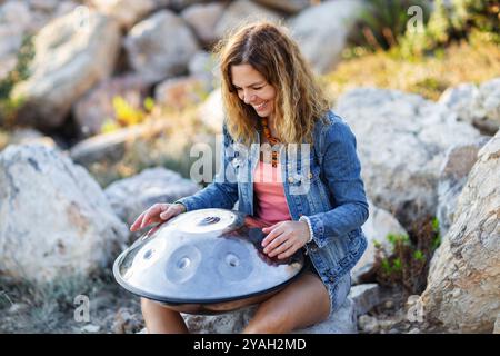 Jeune femme joyeuse jouant joyeusement handpan sur la pierre Banque D'Images