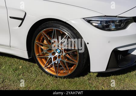 Gros plan d'une roue en alliage de cuivre et d'argent d'une bmw m4 blanche garée sur l'herbe Banque D'Images