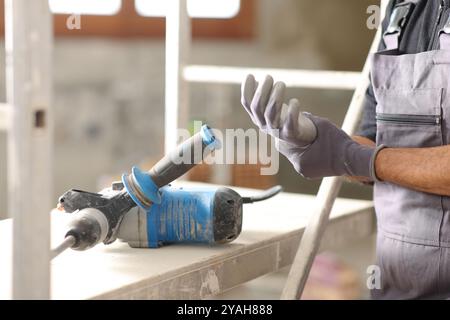 Gros plan d'un travailleur de la construction souffrant de mal de poignet après avoir utilisé un marteau rotatif dans une maison en cours de réforme Banque D'Images