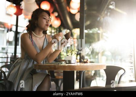 Une jeune femme savoure un cornet de crème glacée dans un café ensoleillé, entouré d'un décor chic et créant une atmosphère urbaine sereine. Banque D'Images