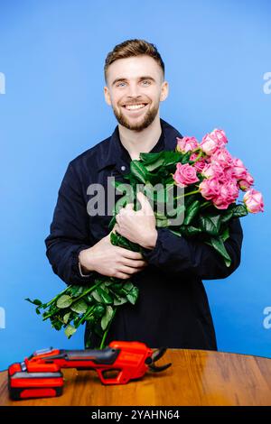 L'homme dans le tablier coupe les extrémités d'une rose sur fond bleu. Banque D'Images