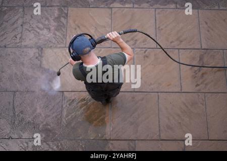 Un homme nettoyant un patio dans un jardin ou une cour arrière avec un nettoyeur haute pression Banque D'Images