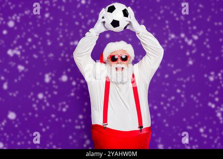 Photo de grey haired santa père holding football ball passer nouvel an nuit à regarder la finale de ligue de champion enthousiaste porter costume specs sun Banque D'Images