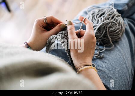 Gros plan des mains tricotant avec du fil gris, en se concentrant sur un artisanat d'hiver confortable. Activité relaxante et consciente pendant les mois les plus froids. Banque D'Images