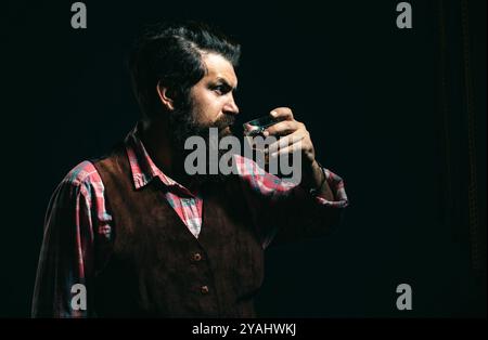 Hipster avec barbe et moustache en costume boit de l'alcool après la journée de travail. Homme riche élégant tenant un verre de vieux whisky. Banque D'Images