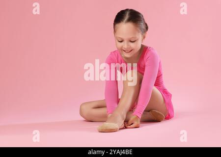 Petite ballerine mettant sur des chaussures pointe sur fond rose, espace pour le texte Banque D'Images