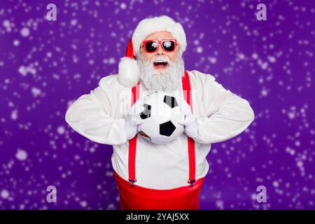 Photo de grey haired santa père holding football ball passer nouvel an nuit à regarder la finale de ligue de champion enthousiaste porter costume specs sun Banque D'Images