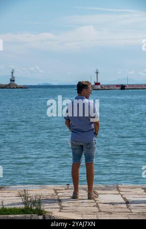 homme debout seul regardant vers la mer sur un quai ou côté port portant des vêtements d'été. Banque D'Images